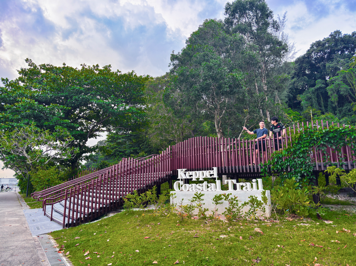Two people on a wooden bridge at Keppel Coastal Trail, surrounded by trees and greenery.